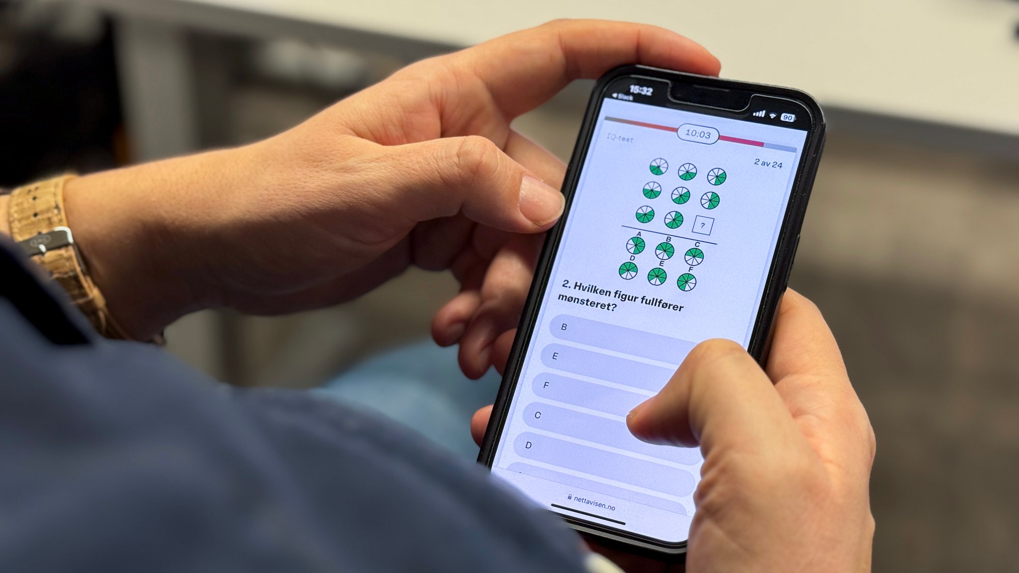 En mann holder en mobiltelefon, og på skjermen vises en evnetest med ulike figurer. 