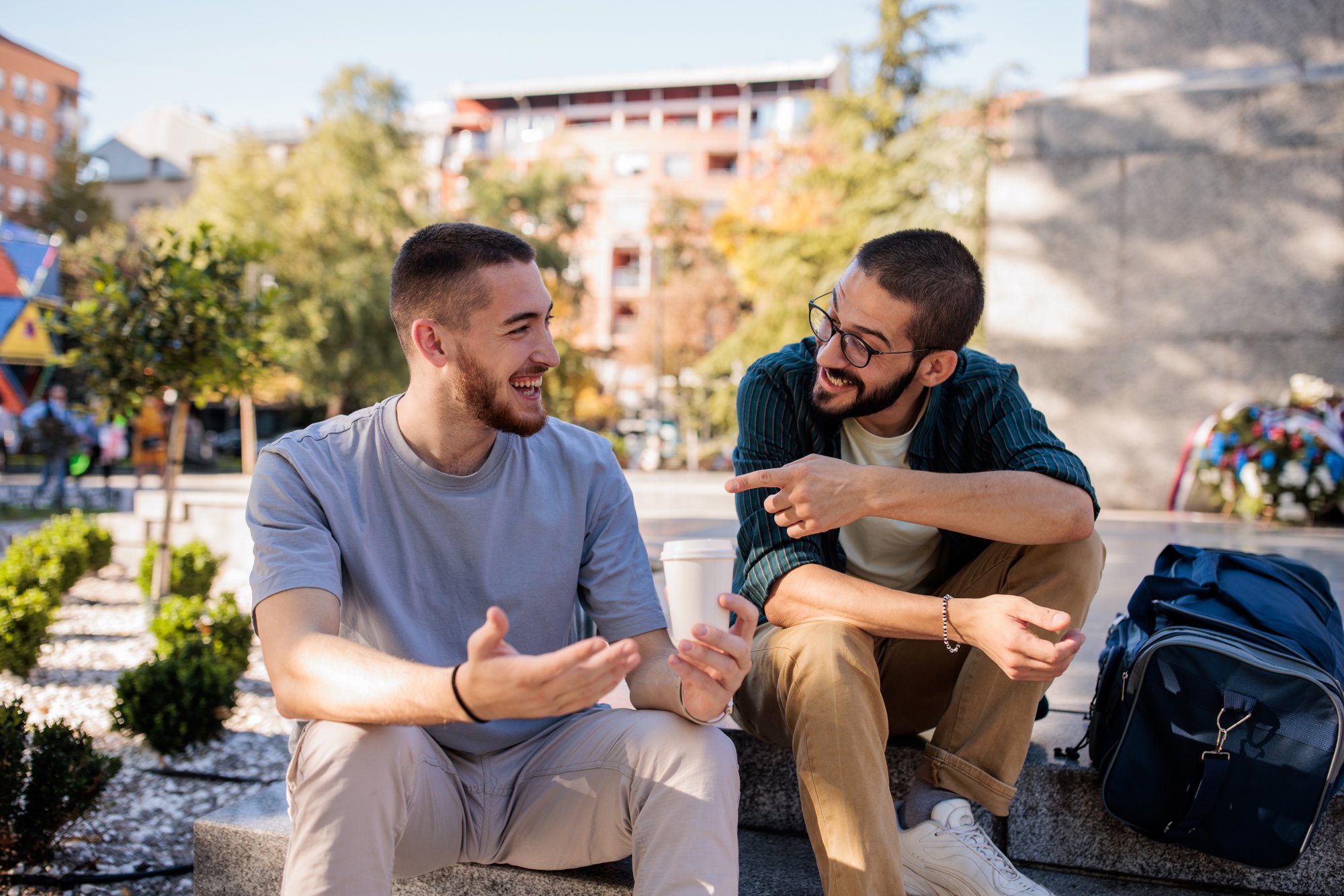 Two male friends talking while sitting on concrete steps in the park in city.
