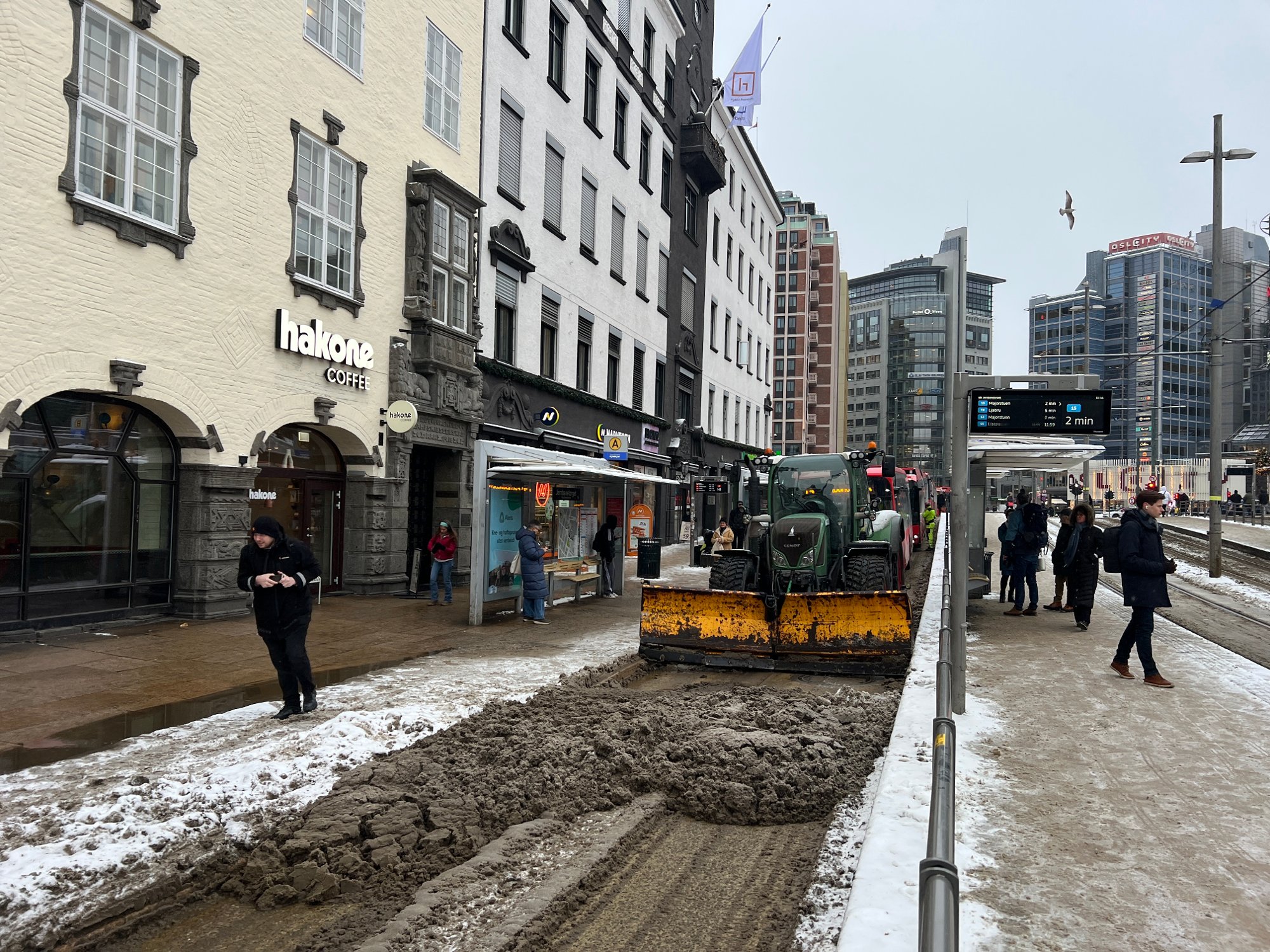 Brøytebil har stanset midt på Jernbanetorget. Bussene står oppover gata